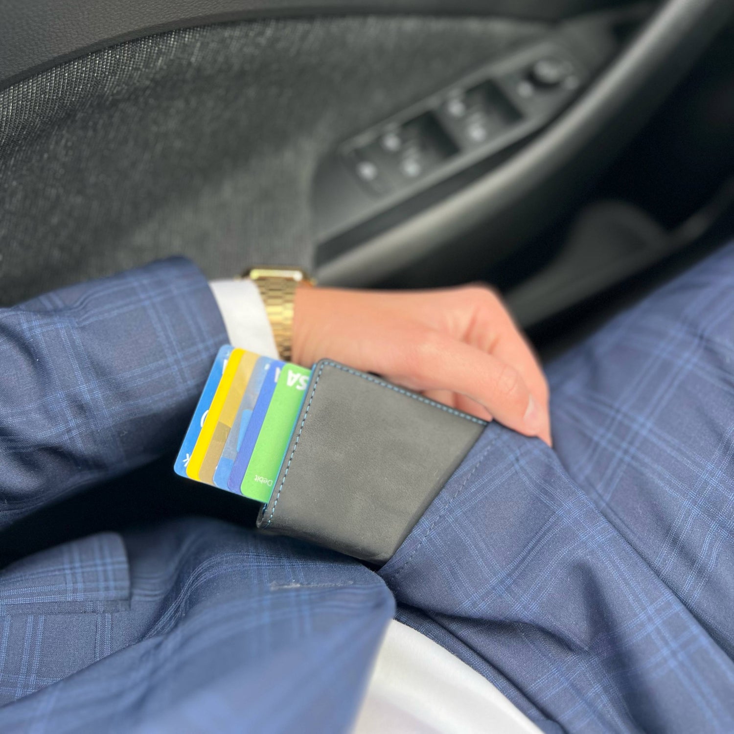 Person holding a black smart wallet with colorful cards inside a car.